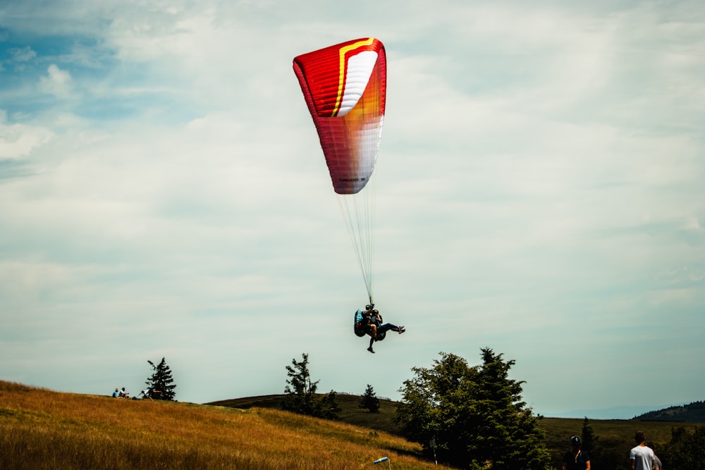 a person is parasailing over a grassy hill