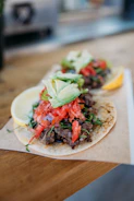Close-up of a sizzling street taco with fresh cilantro and lime on a rustic wooden table.