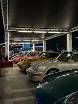 Wide-angle view of a car show with colorful vehicles lined up under bright lights.