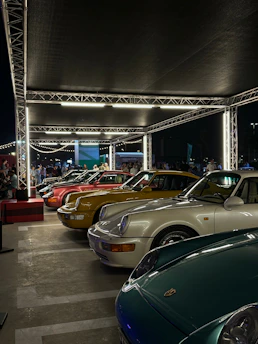 Wide-angle view of a car show with colorful vehicles lined up under bright lights.