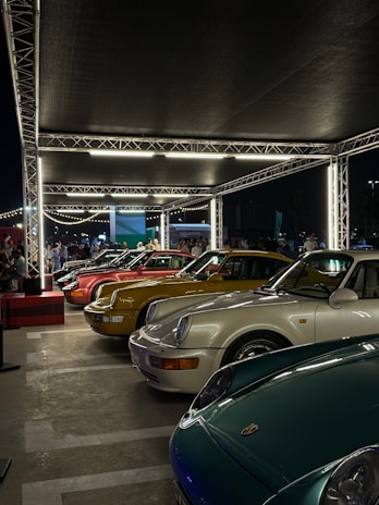 Evening scene of a car show with classic cars illuminated by soft lights, creating a warm and inviting atmosphere for visitors.