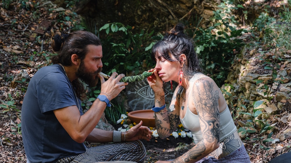 a man and a woman sitting on the ground in the woods