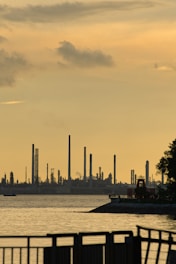 A dynamic handshake silhouette against a backdrop of refinery towers and sprawling crop fields under a setting sun.