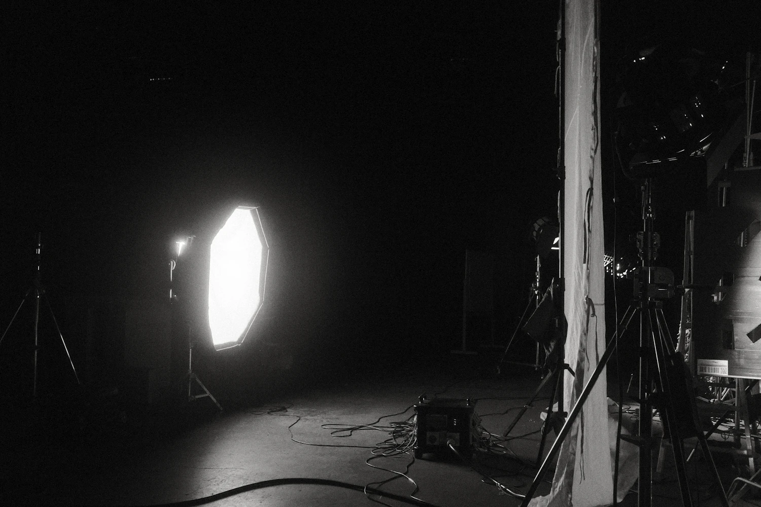A single large softbox burning in an otherwise dark hall, cables running across the floor