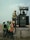 Several workers wearing safety vests and helmets are gathered around an industrial transformer. One person is elevated and appears to be working on the transformer, while others observe and assist from the ground. The setting suggests an outdoor, industrial or construction site.