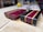 Two rectangular wooden blocks rest on a light-colored surface. The blocks have a striking design with alternating strips of dark brown, deep purple, and light tan wood. The wood appears polished and intricately crafted, with smooth, shiny surfaces and beveled edges.