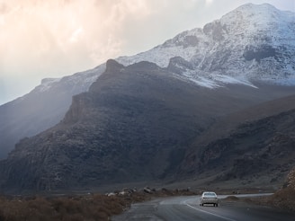 Snow-capped mountains with a sleek SUV driving through a scenic alpine road in the Dolomites.