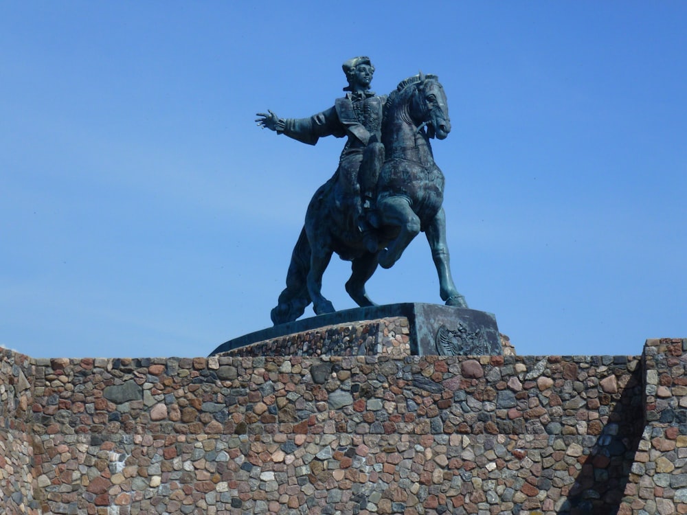 a statue of a man riding a horse on top of a stone wall