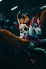 A fantasy action figure depicting a warrior woman with long flowing hair, wearing armor and holding a sword aloft. She rides a winged horse adorned with vibrant colors.