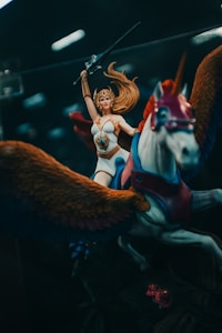A fantasy action figure depicting a warrior woman with long flowing hair, wearing armor and holding a sword aloft. She rides a winged horse adorned with vibrant colors.