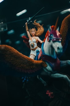 A fantasy action figure depicting a warrior woman with long flowing hair, wearing armor and holding a sword aloft. She rides a winged horse adorned with vibrant colors.