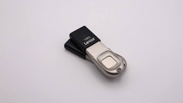 A Lexar USB flash drive, specifically a 128GB model, on a plain white background. The flash drive has a metallic and plastic design, with silver-colored metal and black plastic parts.