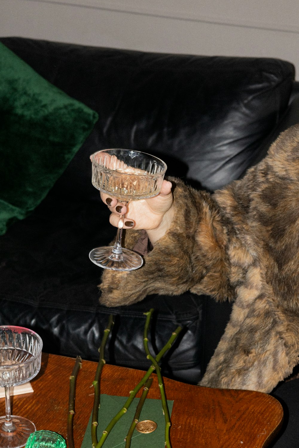 a cat sitting on a couch drinking from a wine glass