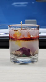 A glass container filled with water and a layer of oil on top, ready for candle making.