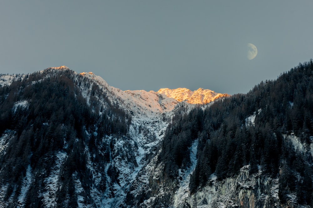 a snowy mountain with a half moon in the sky
