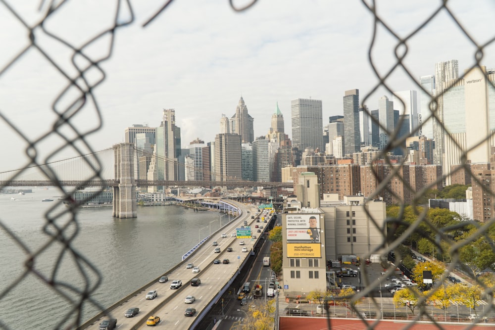 a view of a city and a bridge through a chain link fence