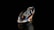 A polished and faceted gemstone, likely a diamond, stands out against a deep black background. The gem's surface reflects and refracts light, creating a spectrum of colors including blues, oranges, and whites across its facets. The overall shape is elongated with precise edges and sharp corners.