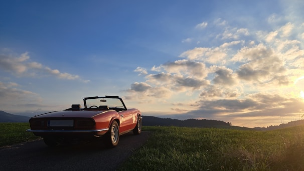 A panoramic view of the rolling hills of Tuscany with a convertible parked by a vineyard.