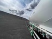 A large tanker vehicle is situated on a barren, rocky landscape under a partly cloudy sky. The tanker appears white with green hoses and is parked on an expansive terrain that is mostly devoid of vegetation or other structures.
