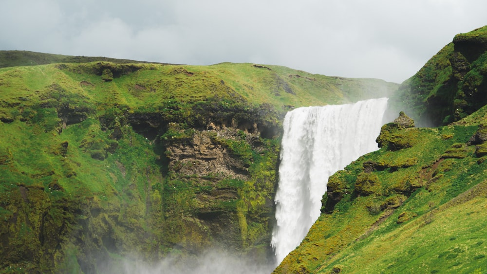a very tall waterfall in the middle of a lush green field