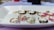 A collection of gold wire rings displayed on a white rectangular dish. Some rings feature colorful beads, including pastel pink, green, and black, with designs appearing delicate and ornamental.