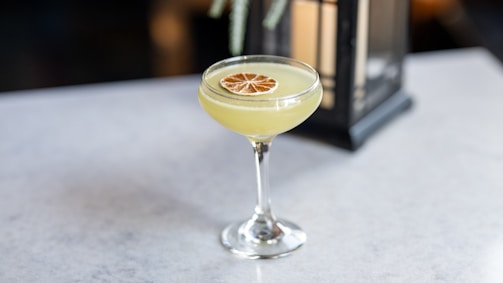 An elegant cocktail glass with a smoky garnish resting on a slate coaster.