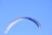 A man landing gently with a colorful paraglider against a bright blue sky.