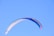 A man landing gently with a colorful paraglider against a bright blue sky.