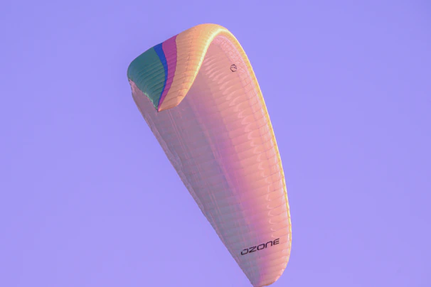A colorful canopy fully deployed, gliding smoothly over a lush green dropzone landscape.