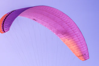 A colorful canopy fully deployed against a backdrop of clear blue sky, with a skydiver gracefully steering.