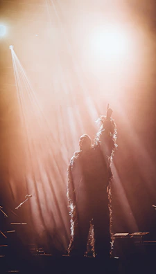 An artist in costume, illuminated by warm stage lights, preparing for their role.