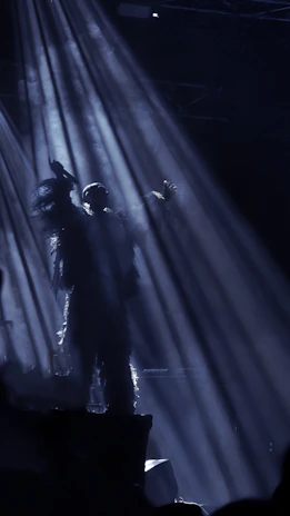 Angled shot of Profit Elijah performing on a dim stage, the spotlight framing his silhouette amid rising smoke.