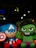 Two plush toys resembling superhero characters with one in blue and red, holding a shield, and another in green with an angry expression. They are displayed against a dark background with some blurred lights.