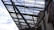 Steel beams and rods form a complex, geometric lattice structure above a modern architectural building. The sky visible in the background is partly cloudy, providing contrast to the industrial elements.