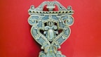 An intricately carved wooden object with floral patterns, ornate scrolls, and symmetrical design against a solid red background. The craftsmanship displays a vintage and artistic feel, with attention to detail in the carvings.