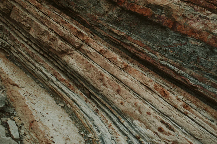 Zbliżenie na naturalne warstwy skalne o różnych odcieniach, ukazujące uwarstwienie geologiczne odsłonięte w przekroju — dokładnie to, co pokazuje profil litologiczny z odwiertu przed rozpoczęciem wiercenia studni.