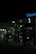 A dimly lit gas station at night featuring several gas pumps under a canopy with the logo partially visible. The station is mostly dark, with some interior lighting emanating from the convenience store in the background.