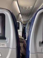 An airplane cabin showing passengers comfortably viewing interactive adverts on back screens.