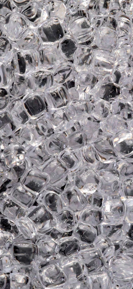Close-up of sparkling, clear ice cubes neatly stacked in a transparent bag, reflecting ambient light.