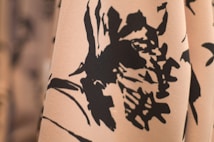 A close-up of fabric featuring a black floral pattern on a light beige background. The design is abstract, with large, bold brushstrokes creating a stark contrast between the dark flowers and the soft backdrop.