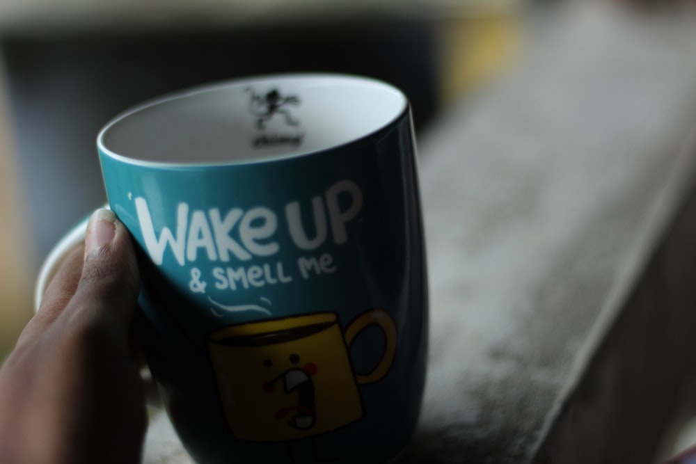 a person holding a coffee cup with the words wake up and smell me on it