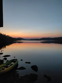 a kayak sitting on the shore of a lake at sunset