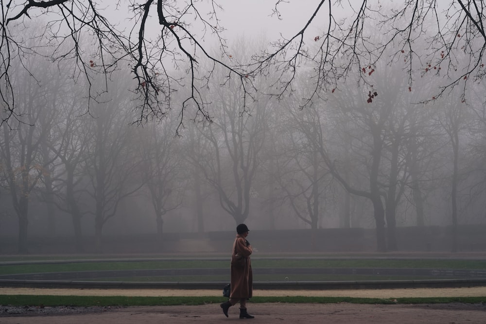 a woman walking through a park on a foggy day