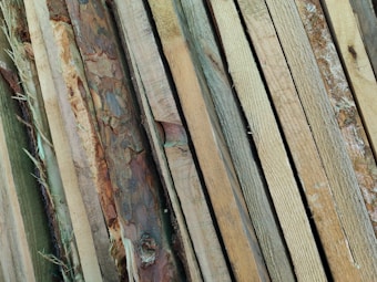 A collection of wooden planks with various textures and colors, ranging from light beige to dark brown, laid out side by side in an overlapping pattern.