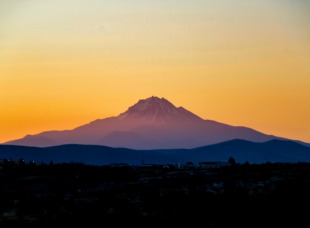 a mountain is silhouetted against a sunset sky