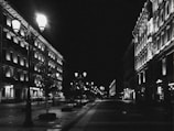 Black and white photograph of an old city street illuminated by lamplight.