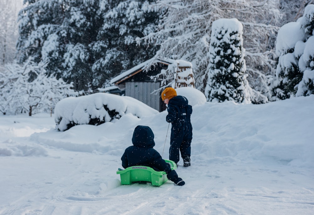 two children playing in the snow on a sled