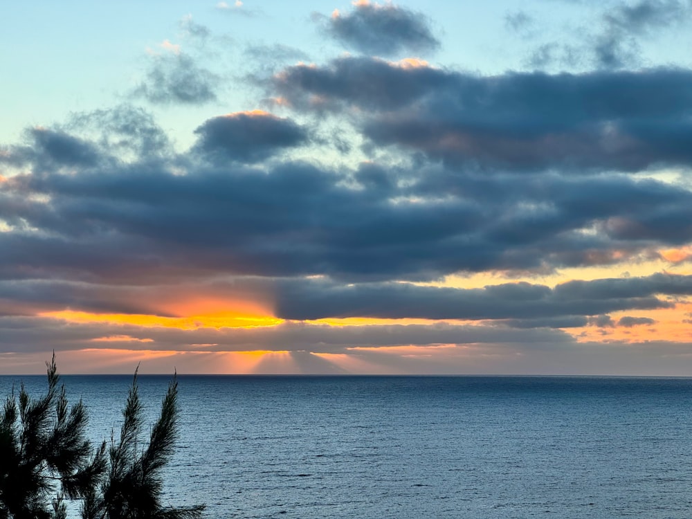 the sun is setting over the ocean on a cloudy day