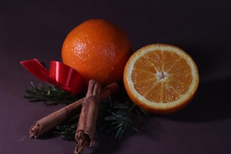 an orange, cinnamon sticks, and an orange on a purple background