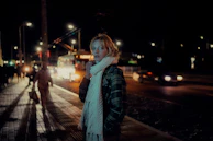 A sunlit city street scene featuring a woman in a tailored cream blazer and soft cashmere scarf.